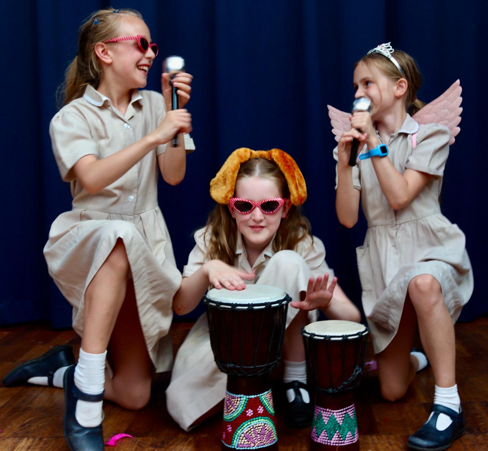 Three girls in fancy dress playing drums on stage